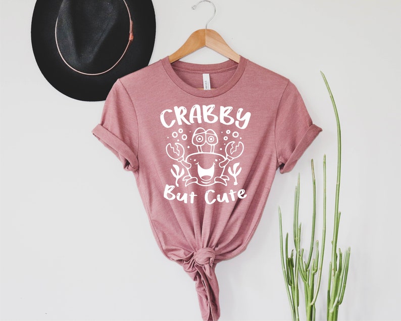 May include: A pink t-shirt with a white graphic of a crab with the text "Crabby But Cute".