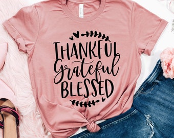 May include: A mauve t-shirt with the text "Thankful Grateful Blessed" in black script lettering. The text is surrounded by small hearts and leaf designs.