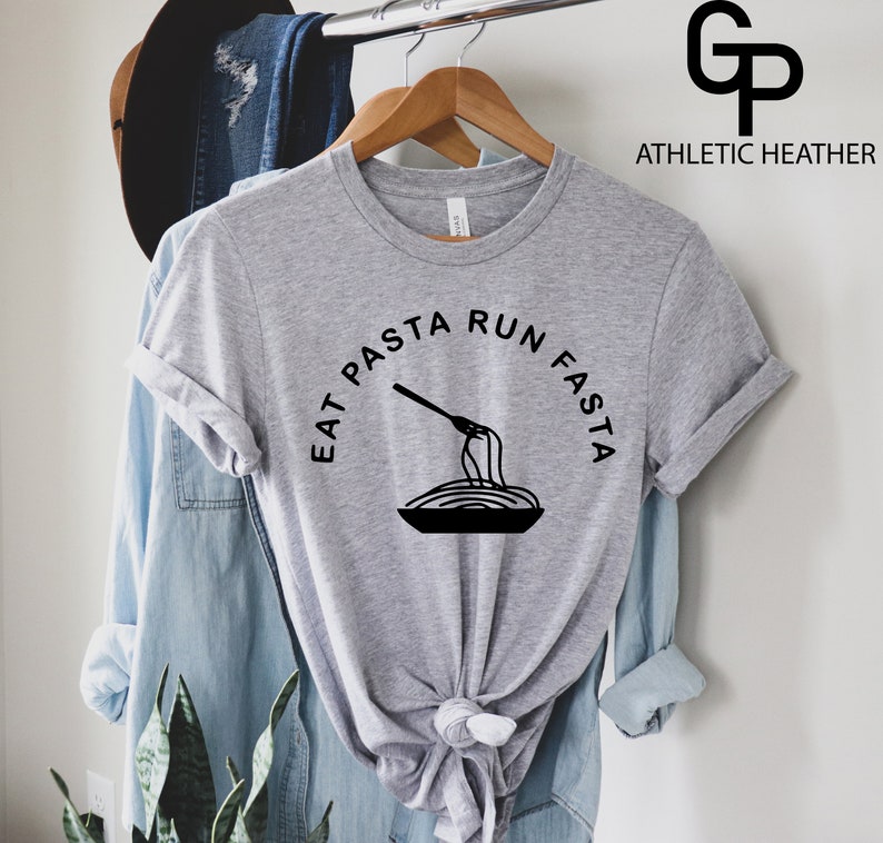 Może przedstawiać: Szary T-shirt z napisem "Eat Pasta Run Fasta" w czarnym kolorze. Na środku koszulki znajduje się czarno-biała ilustracja widelca obracającego spaghetti.