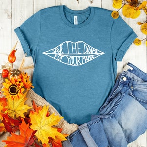 May include: A teal blue t-shirt with a white graphic of a pair of lips with the text "Save the drama for your mama" inside.