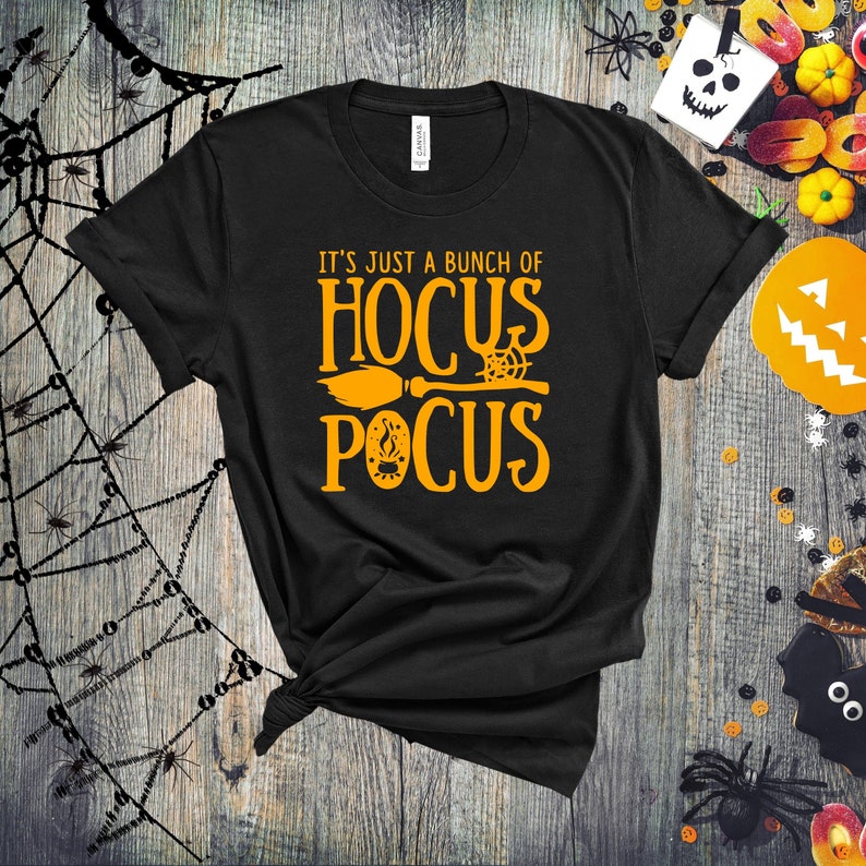 May include: Black t-shirt with the text "It's just a bunch of Hocus Pocus" in orange. A broom and a spiderweb are included in the design.