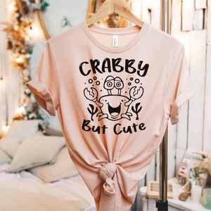 May include: A pink t-shirt with a black graphic of a crab with the text "Crabby But Cute".