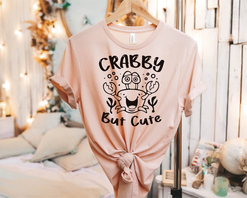 May include: A pink t-shirt with a black graphic of a crab with the text "Crabby But Cute".