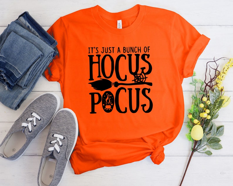 May include: Orange t-shirt with black text that reads "It's just a bunch of Hocus Pocus" with a broom and spider web graphic.