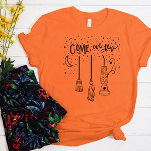 May include: Orange t-shirt with a black graphic of a crescent moon, stars, and three broomsticks with the text "COME, we fly!"