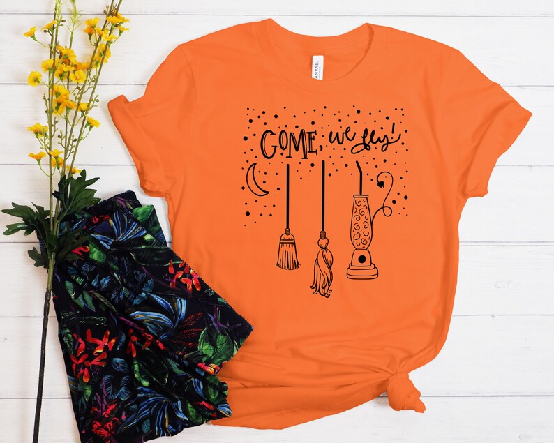 May include: Orange t-shirt with a black graphic of a crescent moon, stars, and three broomsticks with the text "COME, we fly!"