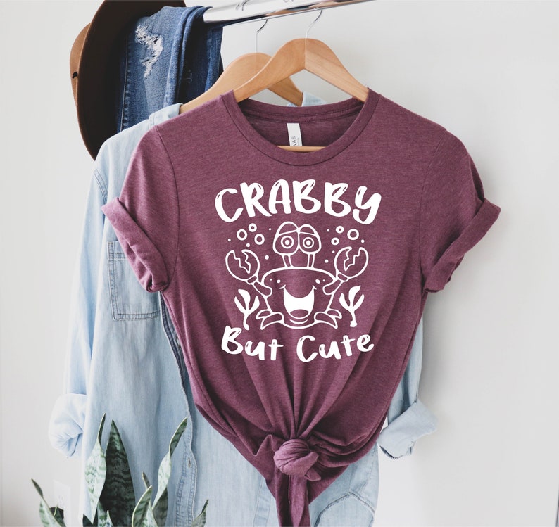 May include: A maroon t-shirt with a white graphic of a crab with the text "Crabby But Cute".