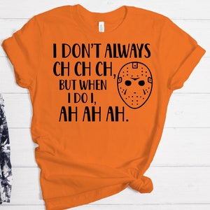 K&ouml;nnte beinhalten: Orangefarbenes T-Shirt mit schwarzem Text, der "Ich mache nicht immer ch ch ch, aber wenn ich es tue, ah ah ah." lautet. Neben dem Text befindet sich eine schwarz-wei&szlig;e Hockeymaske.