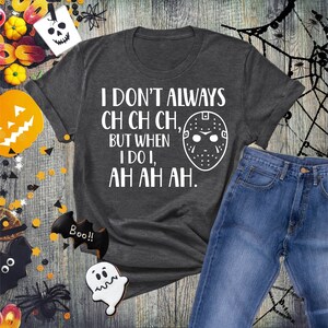 K&ouml;nnte beinhalten: Ein dunkelgraues T-Shirt mit einem wei&szlig;en Grafikdruck, auf dem "Ich mache nicht immer ch ch ch, aber wenn ich es tue, ah ah ah" steht. Die Grafik enth&auml;lt auch eine wei&szlig;e Hockeymaske.