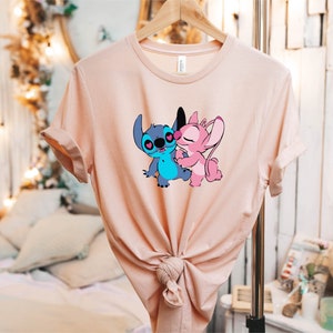 May include: A pink and blue t-shirt with a graphic of Stitch and Angel from the Disney movie Lilo & Stitch. The characters are kissing.