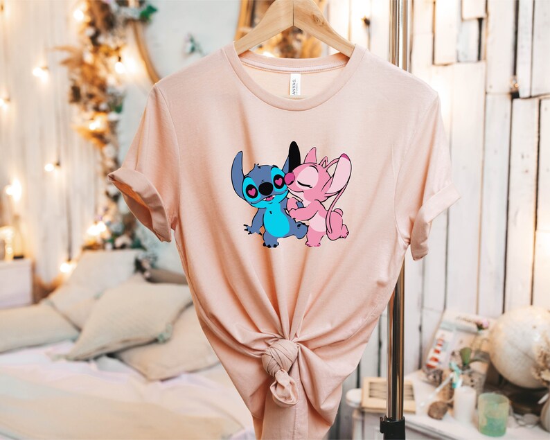May include: A pink and blue t-shirt with a graphic of Stitch and Angel from the Disney movie Lilo & Stitch. The characters are kissing.