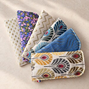 Peut inclure: Un ensemble de six pochettes rectangulaires en tissu disposées en éventail. Les pochettes présentent divers motifs, notamment des gouttes dorées, des imprimés floraux violets et bleus, des zigzags dorés et des plumes de paon.