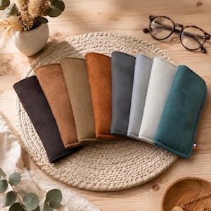 Peut inclure: Un ensemble de huit étuis à lunettes rectangulaires à la texture douce, disposés en éventail. Les étuis présentent une variété de couleurs unies, notamment marron foncé, beige, olive, rouille, anthracite, gris clair, blanc cassé et bleu canard.