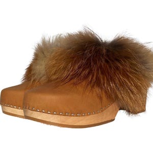 May include: Brown leather clogs with a thick wooden sole and a fluffy brown fur trim around the top.