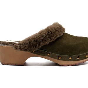 Könnte beinhalten: Grüner Wildlederslipper mit braunem Kunstfellbesatz und einer Holzplattformsohle. Der Slipper hat goldfarbene Metallnieten um die Sohle.