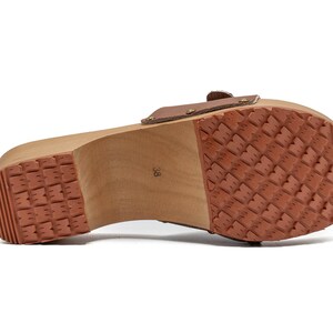 The bottom of a brown leather clog, showing the wooden sole with a textured, reddish-brown rubber tread.