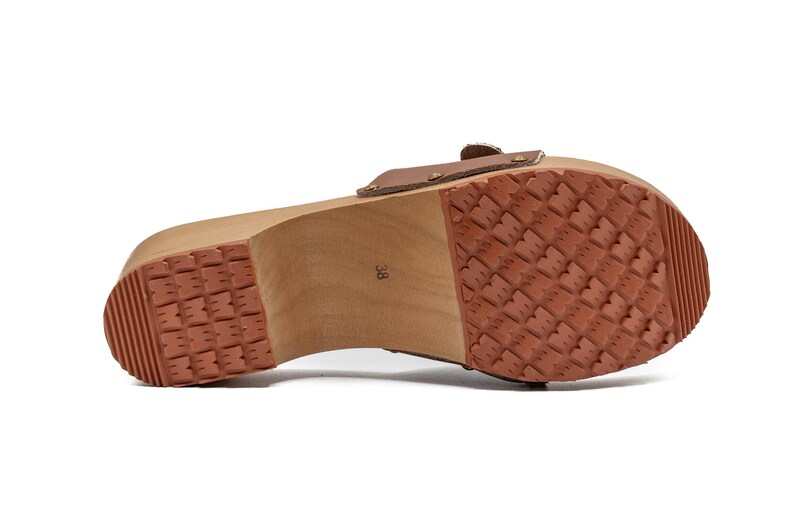 The bottom of a brown leather clog, showing the wooden sole with a textured, reddish-brown rubber tread.