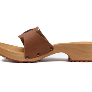A single brown leather clog with a wooden sole and a buckled strap, viewed from the left side.