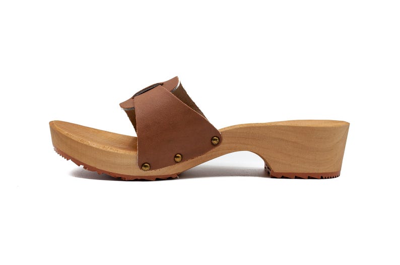A single brown leather clog with a wooden sole and a buckled strap, viewed from the left side.