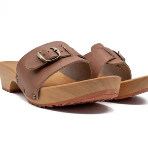 Two brown leather clogs with wooden soles and buckled straps, viewed from a low angle.