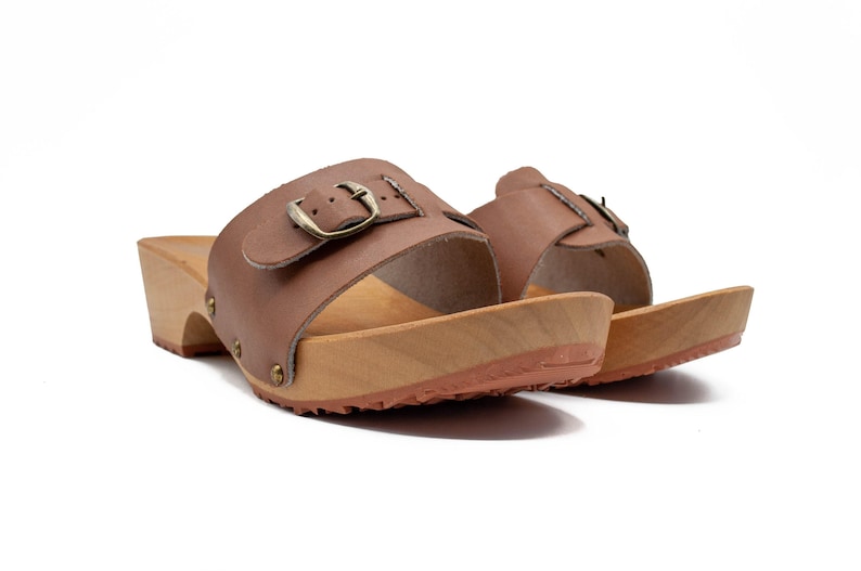 Two brown leather clogs with wooden soles and buckled straps, viewed from a low angle.