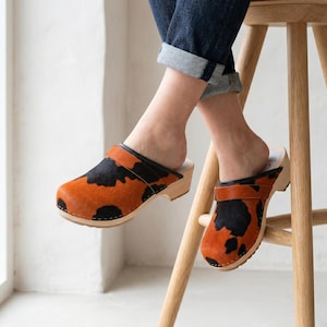 Zuecos de piel con estampado de vaca y suela de madera, calzado cómodo sin cordones.