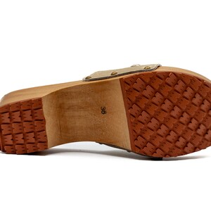 May include: The bottom of a wooden clog with a brown rubber sole. The sole has a textured pattern. The clog is labeled with the size "36".