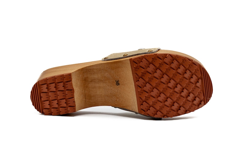 May include: The bottom of a wooden clog with a brown rubber sole. The sole has a textured pattern. The clog is labeled with the size "36".