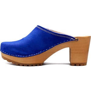 May include: Blue suede clogs with a wooden platform and heel. The clogs have a white stitch detail around the top edge.