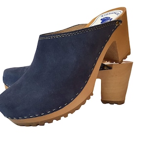 May include: Blue suede clogs with a wooden heel and a stitched seam around the top edge. The clogs have a brown wooden sole with a textured tread.