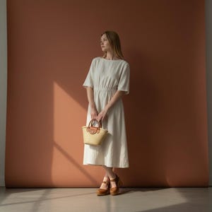 Woman wearing handmade brown leather wooden clogs with ankle strap and block wood heel, styled with cream linen dress against warm neutral background.