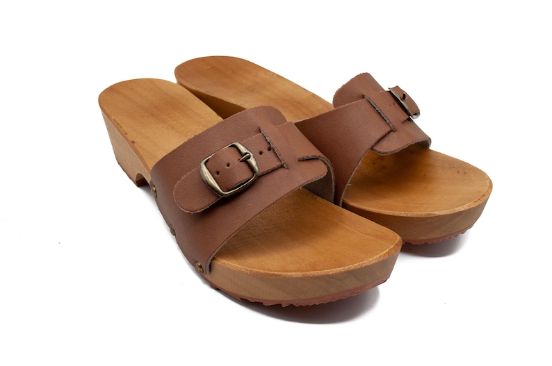 A pair of brown leather clogs with wooden soles and buckled straps, viewed from above and slightly to the front.