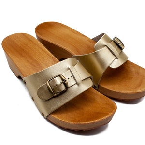 May include: A pair of gold leather sandals with wooden soles and buckles. The sandals have a simple design and are perfect for summer.