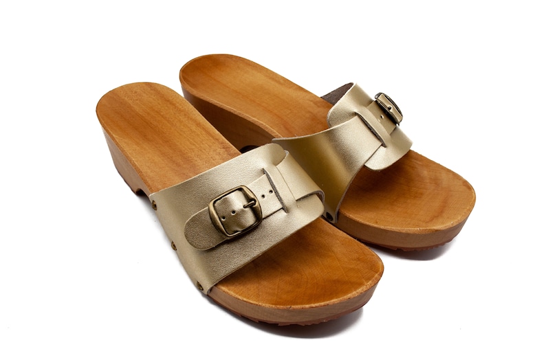 May include: A pair of gold leather sandals with wooden soles and buckles. The sandals have a simple design and are perfect for summer.