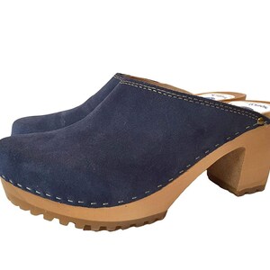 May include: Blue suede clogs with a wooden heel and a stitched seam around the top edge.