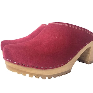May include: Red suede clogs with a wooden platform and a high heel. The clogs have a stitched seam around the top edge.