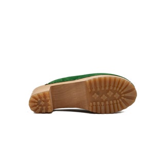 Puede incluir: Zueco de ante verde con plataforma de madera y suela de goma marr&oacute;n.