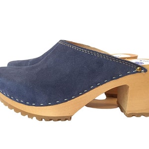 May include: Blue suede clogs with a wooden platform and heel. The clogs have a white stitch detail around the edge of the suede.