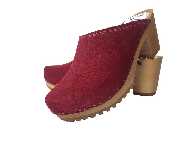 May include: Red suede clogs with a wooden heel and a white stitched trim. The clogs have a textured sole.