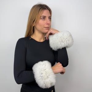 Pode incluir: Uma mulher vestindo uma camisa preta de manga comprida com punhos de pele branca em ambos os pulsos.
