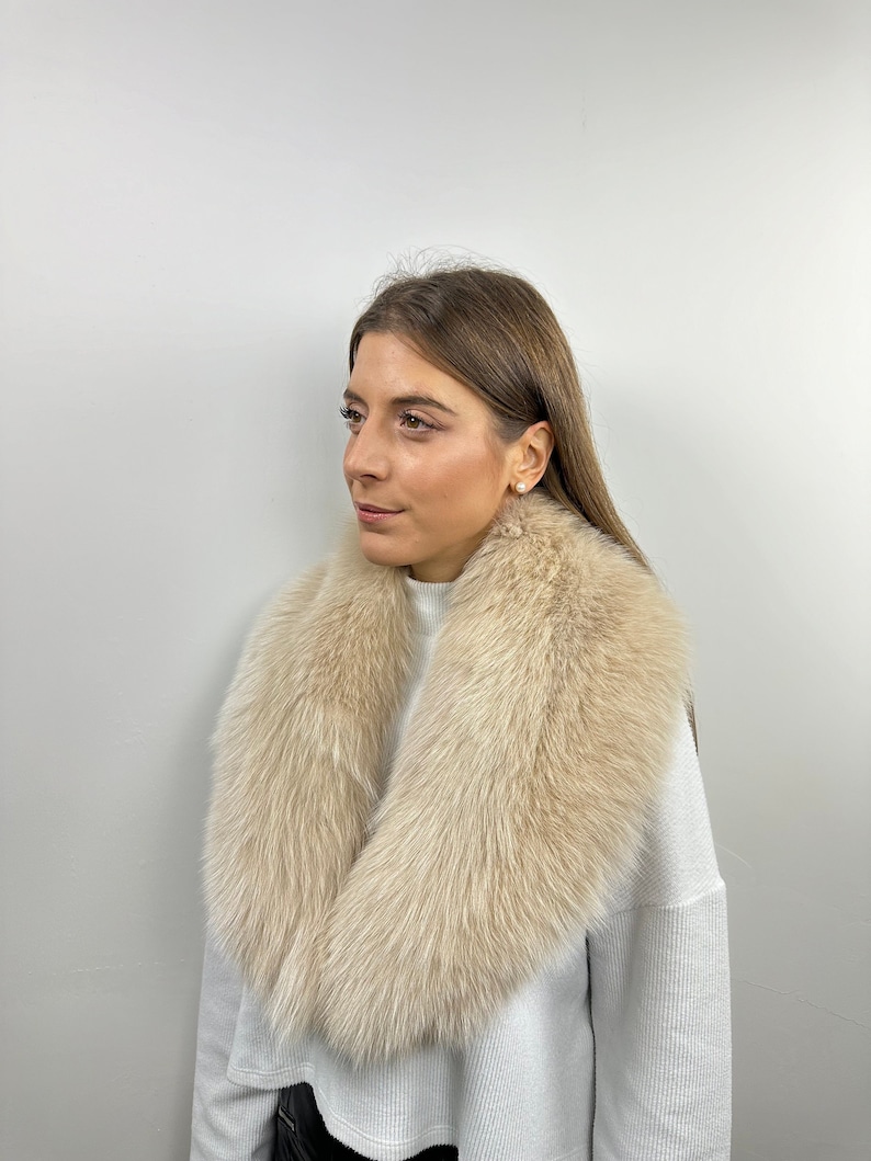 May include: A woman wearing a white sweater with a large, fluffy, cream-colored fur collar.
