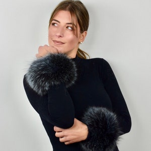 Puede incluir: Una mujer lleva un jersey negro de cuello alto con puños de piel negra en ambas muñecas. Los puños de piel son suaves y esponjosos.