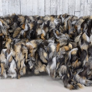 Könnte beinhalten: Eine große, flauschige, mehrfarbige Fuchspelz-Decke. Die Decke besteht aus verschiedenen Farbtönen von braunem, grauem und weißem Fell. Sie ist über ein graues Sofa gelegt.