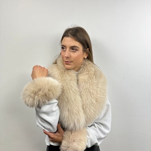 May include: A cream-colored fur scarf with a large collar and matching wrist cuffs. The scarf is made of soft, fluffy fur and is perfect for adding a touch of luxury to any outfit.