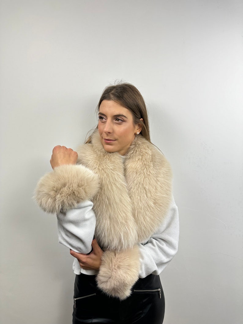 May include: A cream-colored fur scarf with a large collar and matching wrist cuffs. The scarf is made of soft, fluffy fur and is perfect for adding a touch of luxury to any outfit.