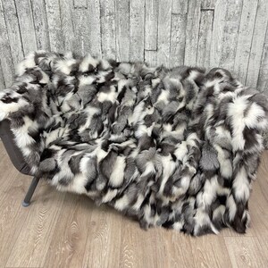 Può includere: Una lussuosa coperta con una miscela di pelliccia grigia, bianca e nera. La coperta è drappeggiata su una sedia grigio scuro, mettendo in risalto la sua consistenza e le variazioni di colore. La pelliccia appare morbida e soffice.