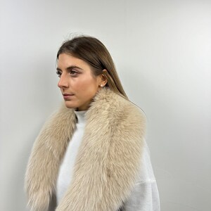 May include: A light beige fur collar with a long, flowing design. The collar is made of soft, fluffy fur and is perfect for adding a touch of luxury to any outfit.