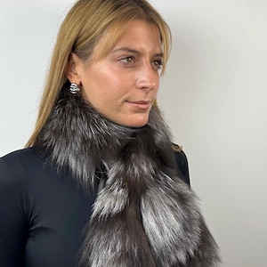 May include: A woman wearing a black turtleneck sweater with a silver fox fur scarf around her neck.