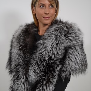 Könnte beinhalten: Ein luxuriöser Stola aus Silberfuchsfell. Das Fell ist eine Mischung aus Schwarz und Silber, was einen auffälligen Kontrast erzeugt. Die Stola ist über den Schultern drapiert und bietet einen glamourösen Look. Der Hintergrund ist schlicht weiß.