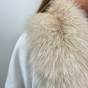 May include: A light beige fur collar with a soft, fluffy texture. The collar is made of real fur and is perfect for adding a touch of luxury to any outfit.